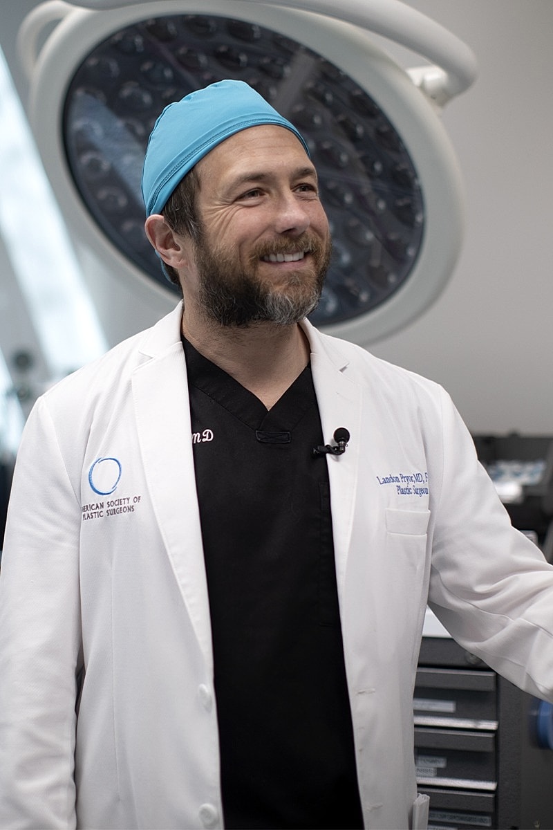 Smiling surgeon wearing scrubs and surgical cap.